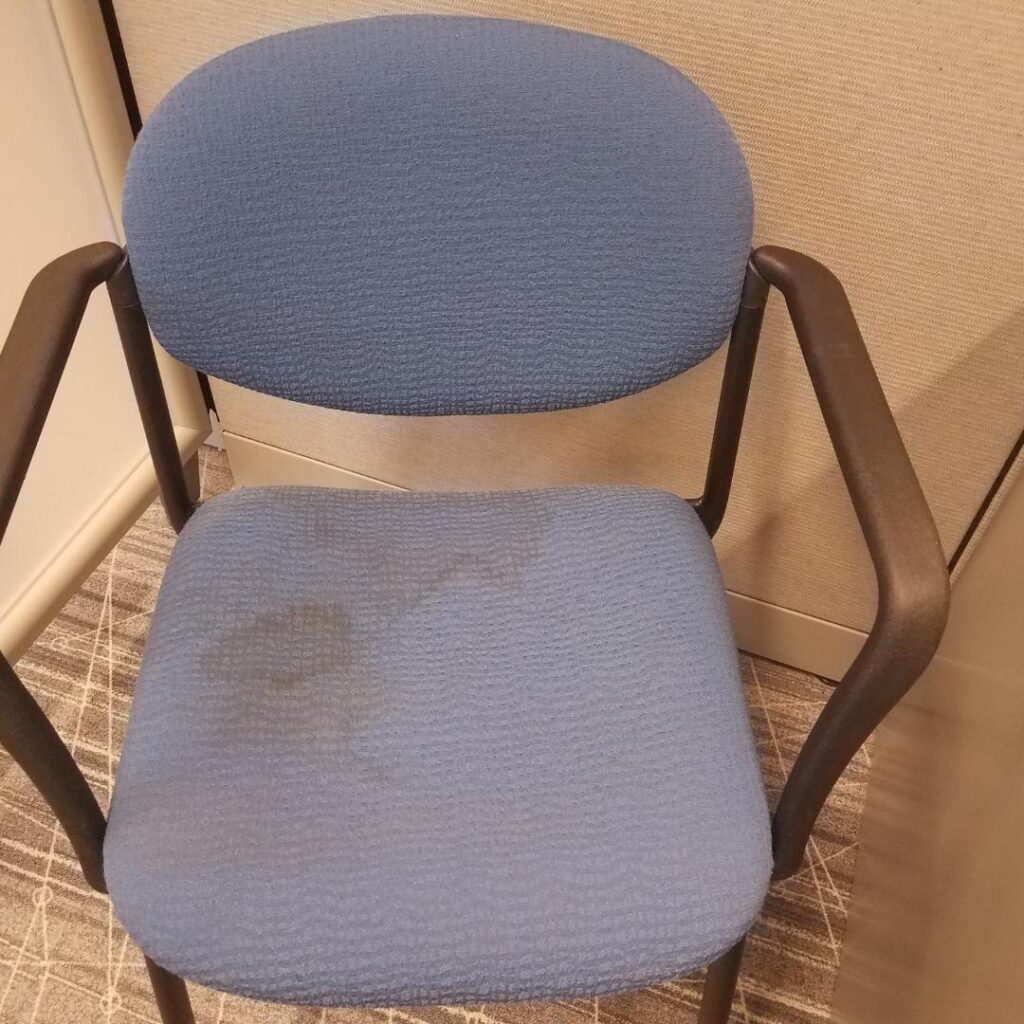 Blue office chair with stains on grey carpet in cubicle